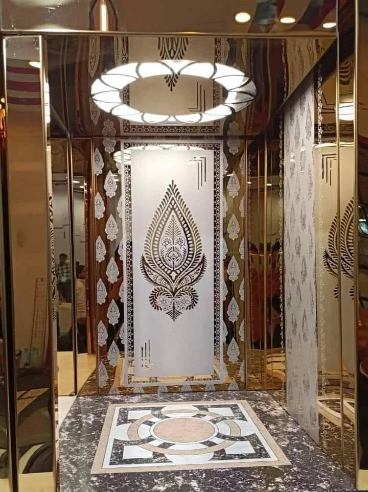 Elevator interior with etched teardrop panels, gold trim, ring ceiling light and a mosaic floor